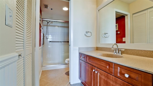 bathroom featuring a shower with door, vanity, tile patterned flooring, and toilet