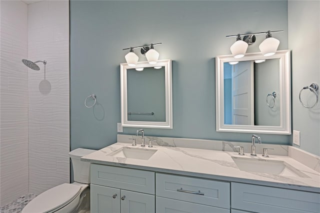 bathroom featuring toilet, a tile shower, and dual vanity