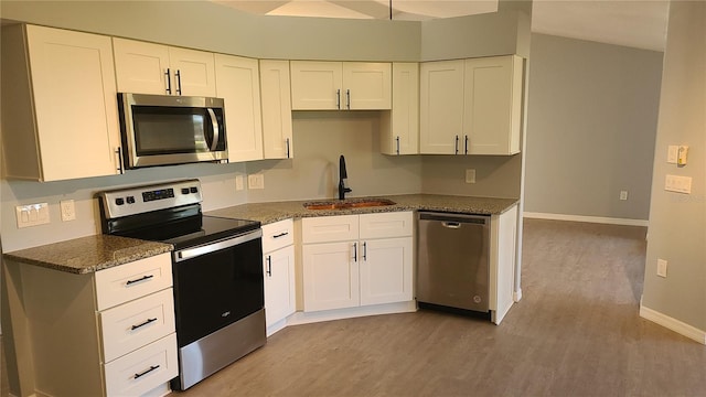 kitchen with white cabinetry, stainless steel appliances, dark stone counters, sink, and light hardwood / wood-style flooring