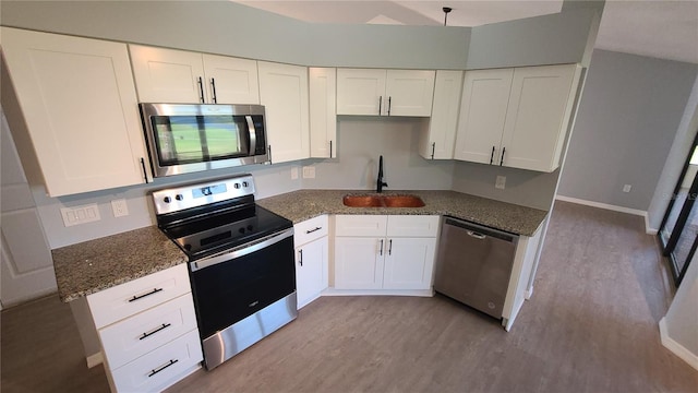 kitchen featuring stainless steel appliances, white cabinets, dark stone counters, light hardwood / wood-style flooring, and sink