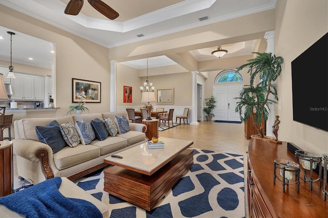 tiled living room with crown molding, ceiling fan with notable chandelier, ornate columns, and a raised ceiling