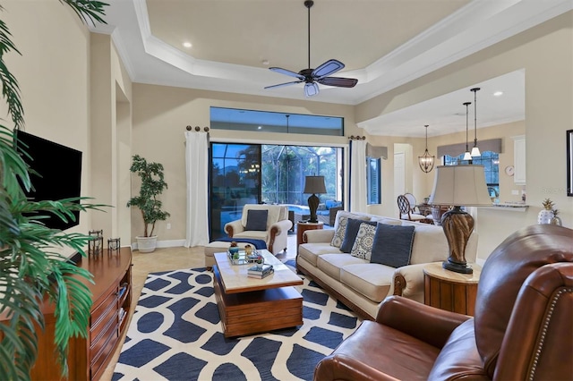 living room featuring ornamental molding, ceiling fan with notable chandelier, and a raised ceiling