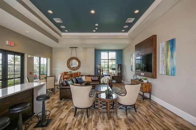 living room with ornamental molding, wood-type flooring, and a raised ceiling