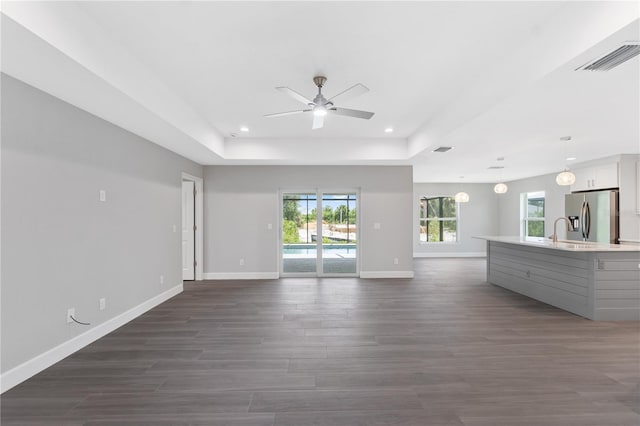 unfurnished living room featuring dark hardwood / wood-style floors, ceiling fan, a tray ceiling, and sink