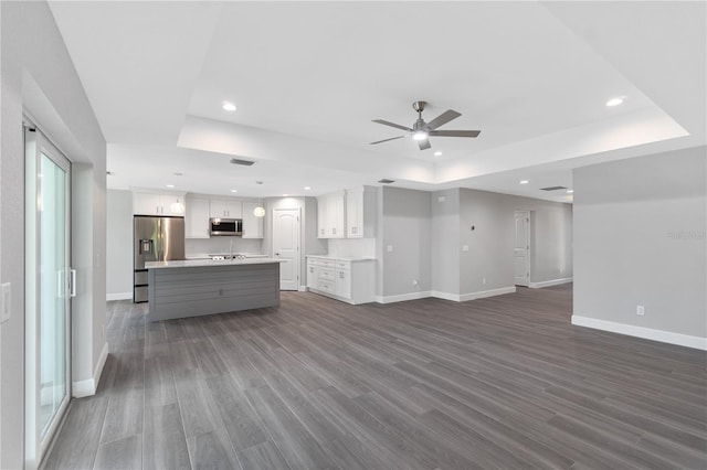 unfurnished living room featuring a tray ceiling, sink, dark wood-type flooring, and ceiling fan