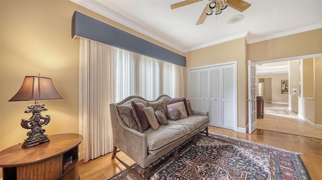 living area with a textured ceiling, light wood-type flooring, ceiling fan, and crown molding