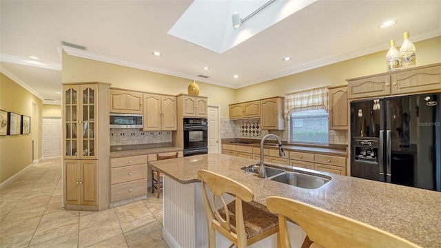 kitchen with a skylight, sink, light brown cabinets, a breakfast bar area, and black appliances