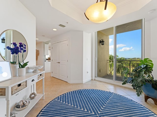 entryway featuring crown molding, a tray ceiling, and light tile patterned floors