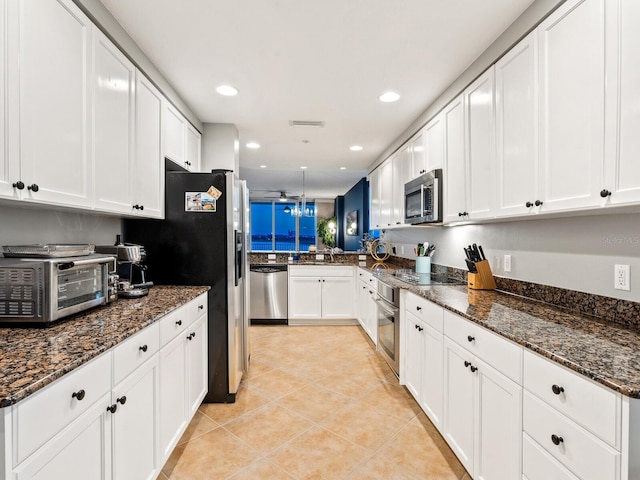 kitchen with appliances with stainless steel finishes, light tile patterned flooring, white cabinetry, and dark stone countertops