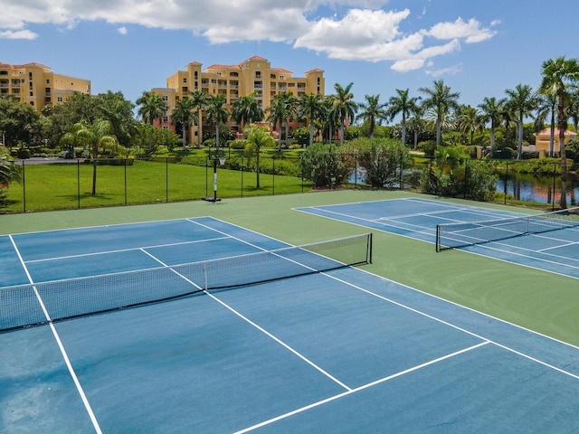 view of tennis court featuring a water view and a lawn