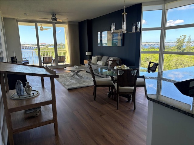 living room featuring dark wood-type flooring, a water view, a wall of windows, and ceiling fan with notable chandelier