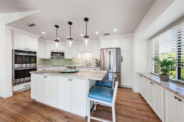 kitchen featuring white cabinets, sink, light stone countertops, decorative light fixtures, and stainless steel appliances