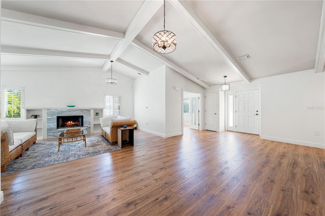 living room featuring hardwood / wood-style flooring, vaulted ceiling with beams, a stone fireplace, and an inviting chandelier