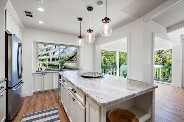 kitchen with a center island, stainless steel fridge, light stone counters, and white cabinetry