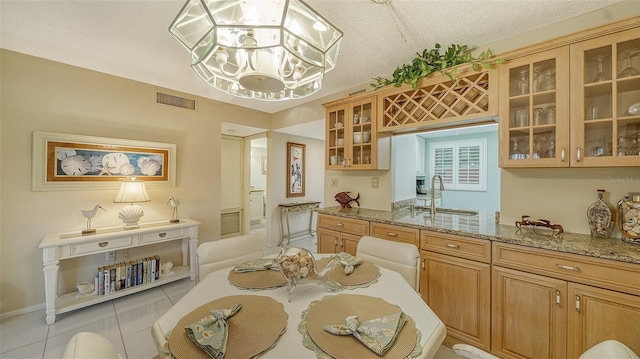 kitchen with sink, light tile floors, light stone counters, a textured ceiling, and a notable chandelier