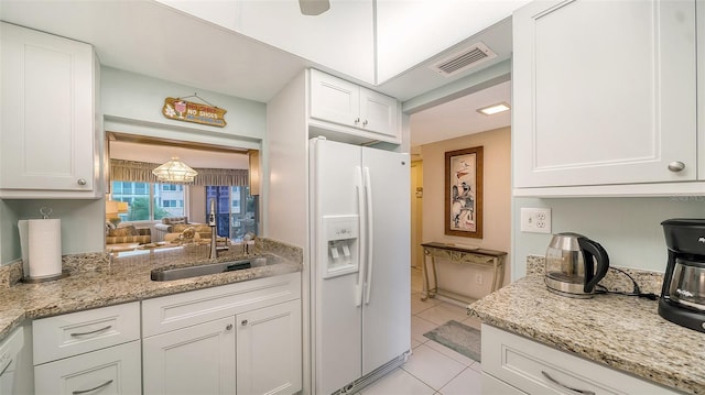 kitchen with white cabinets, white fridge with ice dispenser, light tile floors, and sink