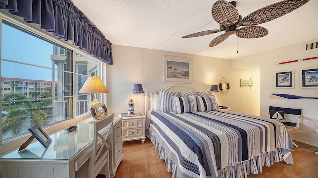 bedroom with a textured ceiling, ceiling fan, and dark hardwood / wood-style flooring