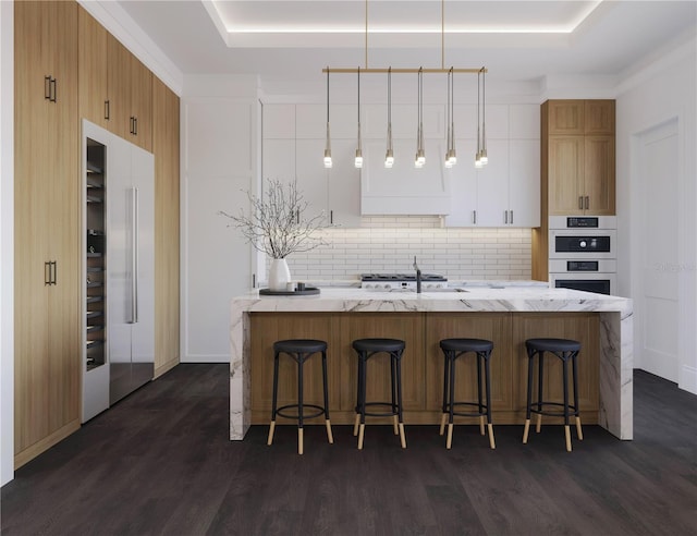 kitchen with hanging light fixtures, high end refrigerator, white cabinets, and a tray ceiling