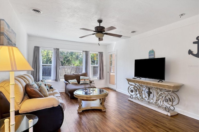 living room with a textured ceiling, ceiling fan, and dark wood-type flooring