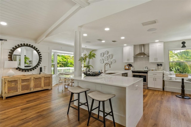 kitchen featuring wall chimney range hood, stainless steel range oven, wood-type flooring, and a wealth of natural light