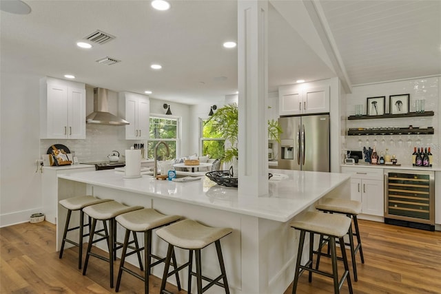 kitchen featuring wine cooler, a kitchen island with sink, hardwood / wood-style floors, wall chimney exhaust hood, and stainless steel refrigerator with ice dispenser