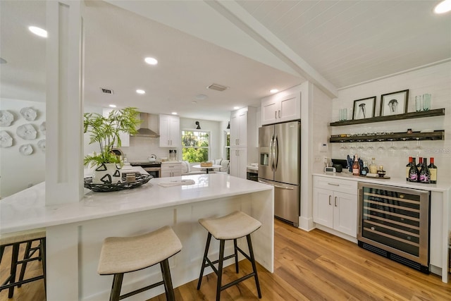 kitchen with appliances with stainless steel finishes, white cabinets, decorative backsplash, beverage cooler, and wall chimney exhaust hood