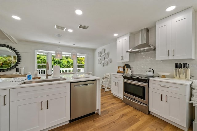 kitchen with white cabinetry, light wood-type flooring, backsplash, stainless steel appliances, and wall chimney exhaust hood