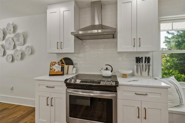 kitchen with white cabinetry, electric stove, tasteful backsplash, wall chimney range hood, and hardwood / wood-style floors