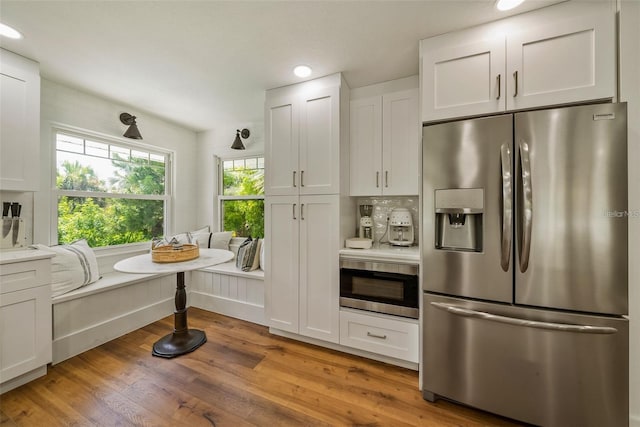 kitchen with light hardwood / wood-style floors, white cabinets, oven, stainless steel fridge, and backsplash