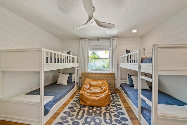 bedroom featuring a textured ceiling, wood-type flooring, ceiling fan, and wood walls