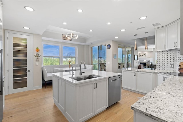 kitchen with sink, light hardwood / wood-style flooring, stainless steel dishwasher, decorative light fixtures, and white cabinets