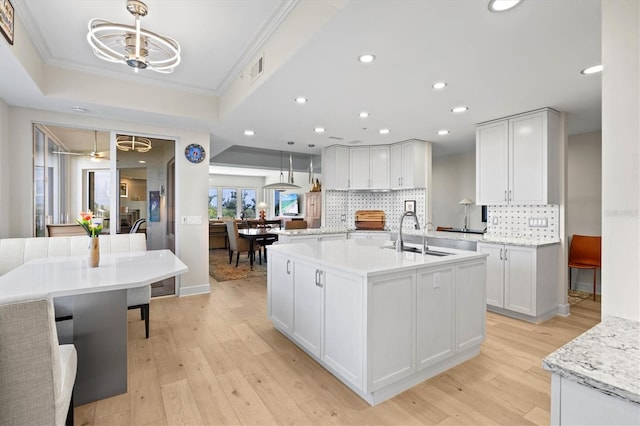 kitchen with sink, crown molding, hanging light fixtures, light wood-type flooring, and white cabinetry