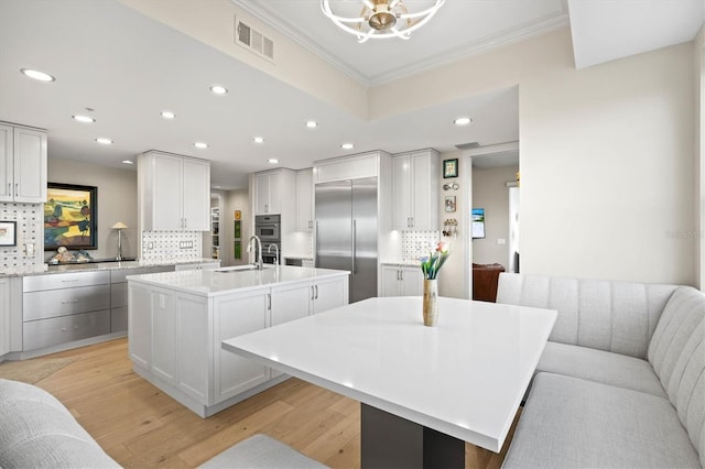 kitchen featuring crown molding, decorative backsplash, light wood-type flooring, an island with sink, and stainless steel appliances