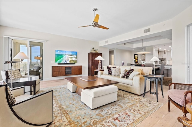 living room featuring light hardwood / wood-style floors, ceiling fan, and a tray ceiling