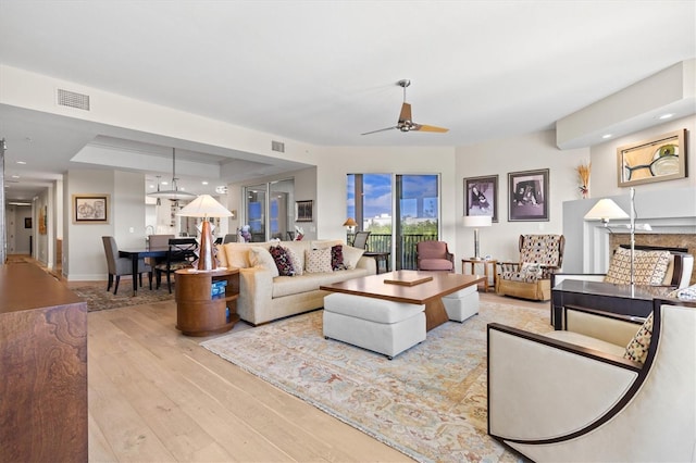 living room featuring ceiling fan, light wood-type flooring, and a tray ceiling