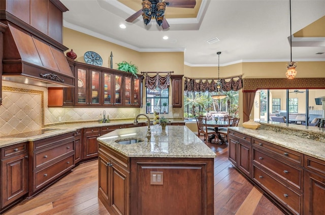 kitchen with hanging light fixtures, custom range hood, sink, and a center island with sink