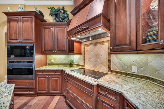 kitchen featuring premium range hood, light stone counters, ornamental molding, black appliances, and light wood-type flooring