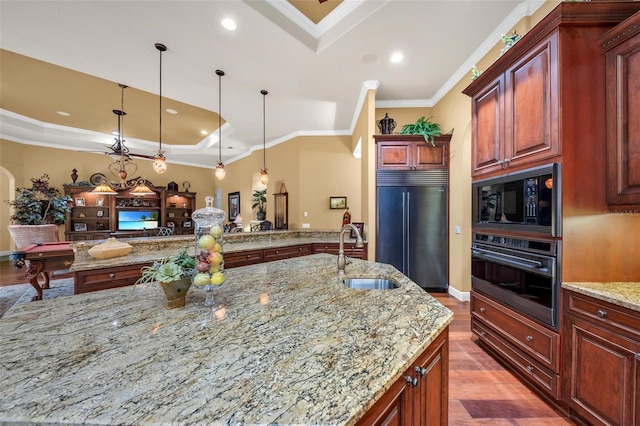 kitchen featuring pendant lighting, sink, built in appliances, light stone counters, and a tray ceiling