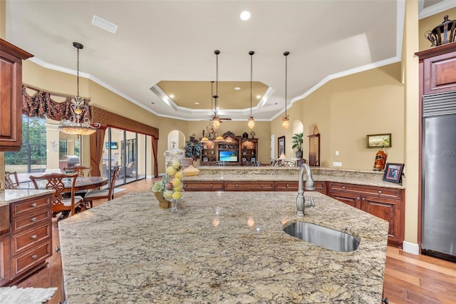 kitchen featuring decorative light fixtures, an island with sink, sink, stainless steel fridge, and light stone counters