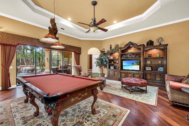 recreation room with dark wood-type flooring, a tray ceiling, and crown molding