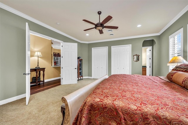 carpeted bedroom with multiple closets, crown molding, and ceiling fan