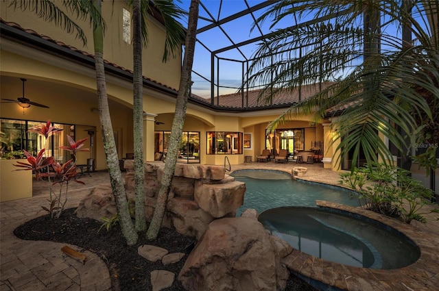 pool at dusk featuring a lanai, a patio, ceiling fan, and an in ground hot tub