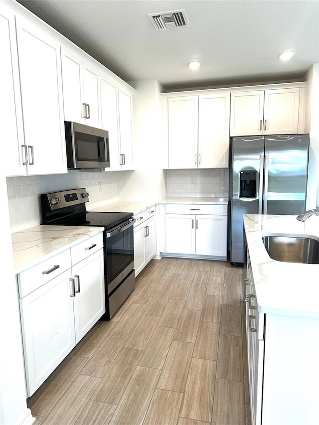 kitchen featuring sink, decorative backsplash, light hardwood / wood-style floors, white cabinetry, and stainless steel appliances