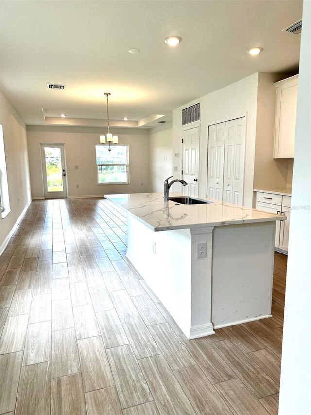 kitchen featuring a large island with sink, light hardwood / wood-style floors, white cabinetry, and sink