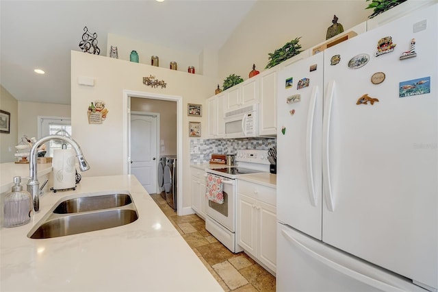 kitchen featuring washing machine and clothes dryer, white appliances, white cabinetry, and sink