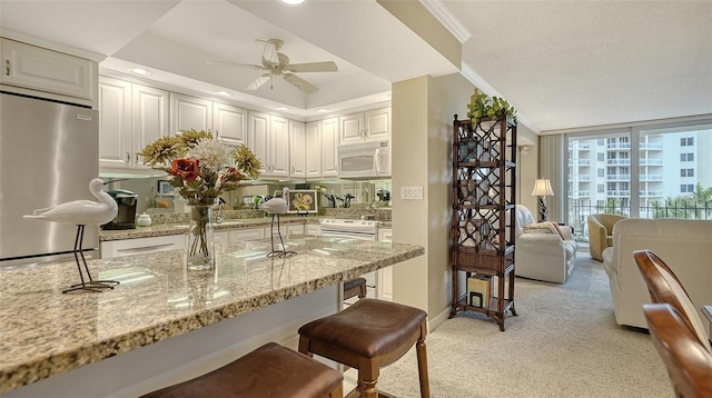 kitchen with a breakfast bar, white appliances, white cabinets, ceiling fan, and light stone countertops