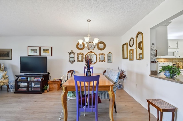 dining area featuring light hardwood / wood-style floors, a textured ceiling, and an inviting chandelier