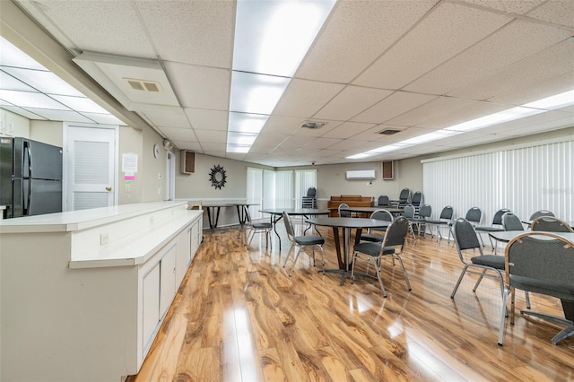 kitchen with white cabinets, a paneled ceiling, black fridge, and light hardwood / wood-style flooring