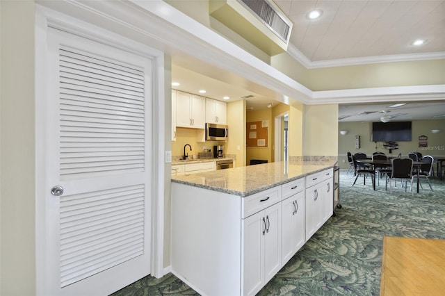 kitchen with white cabinetry, ceiling fan, light stone counters, crown molding, and dark carpet