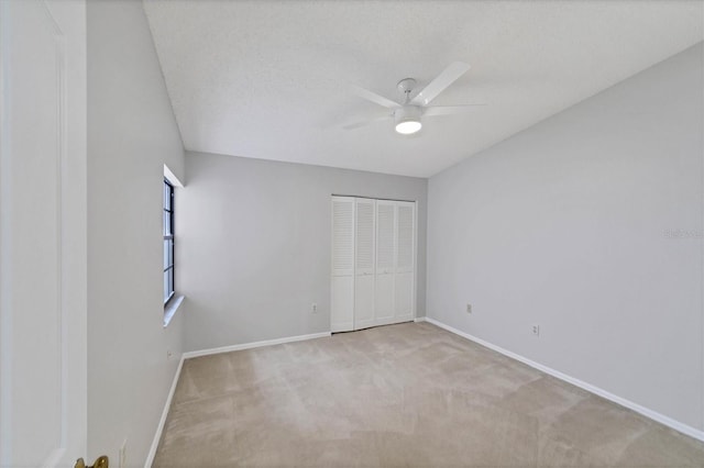 unfurnished bedroom featuring light carpet, a textured ceiling, a closet, and ceiling fan